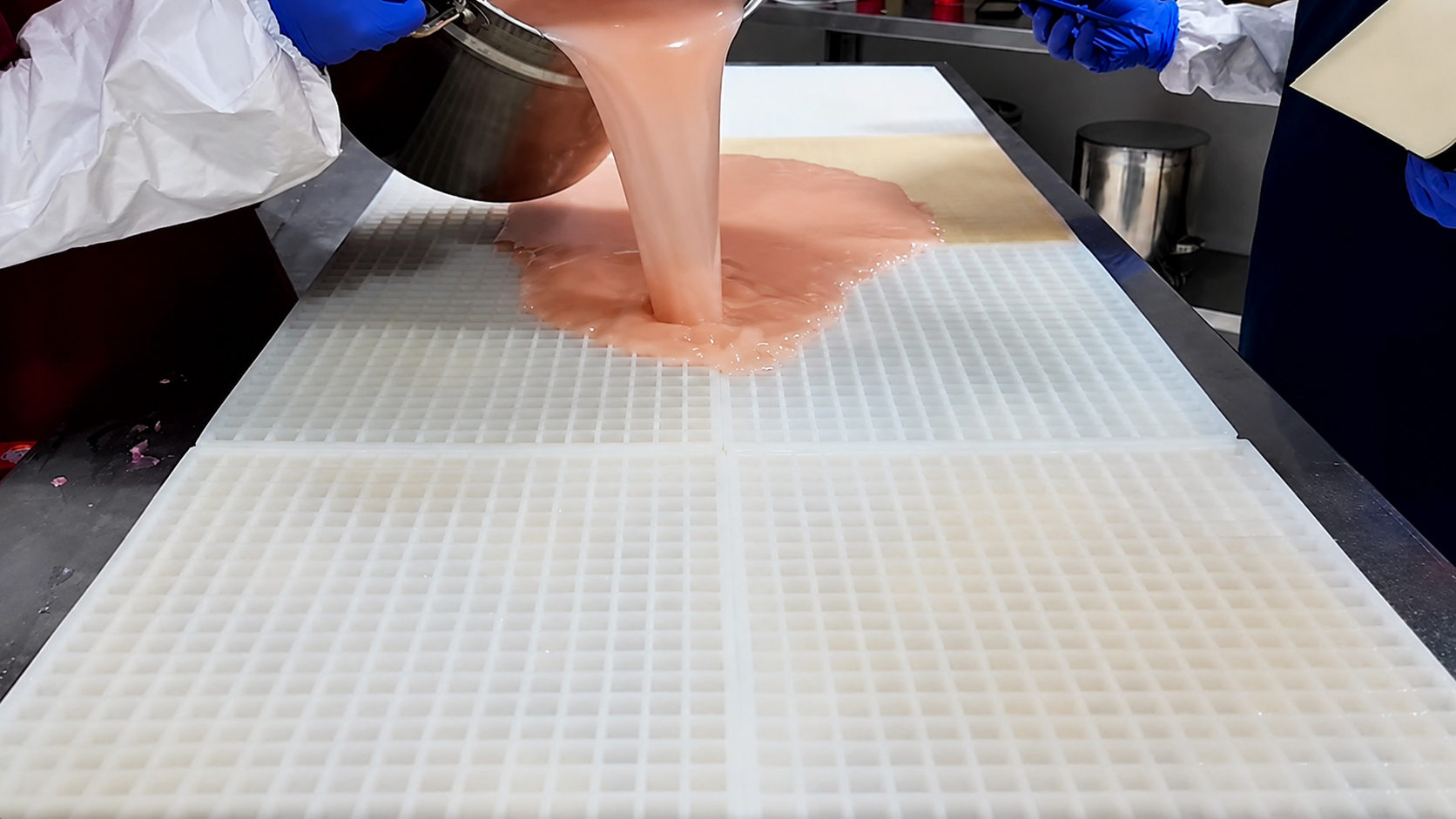 Gummy Molds team pouring gummy mixture across a large commercial silicone gummy mold before scraping